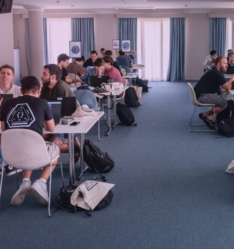 Persone di moveax che lavorano ai laptop, sedute a piccoli tavoli in una grande sala luminosa