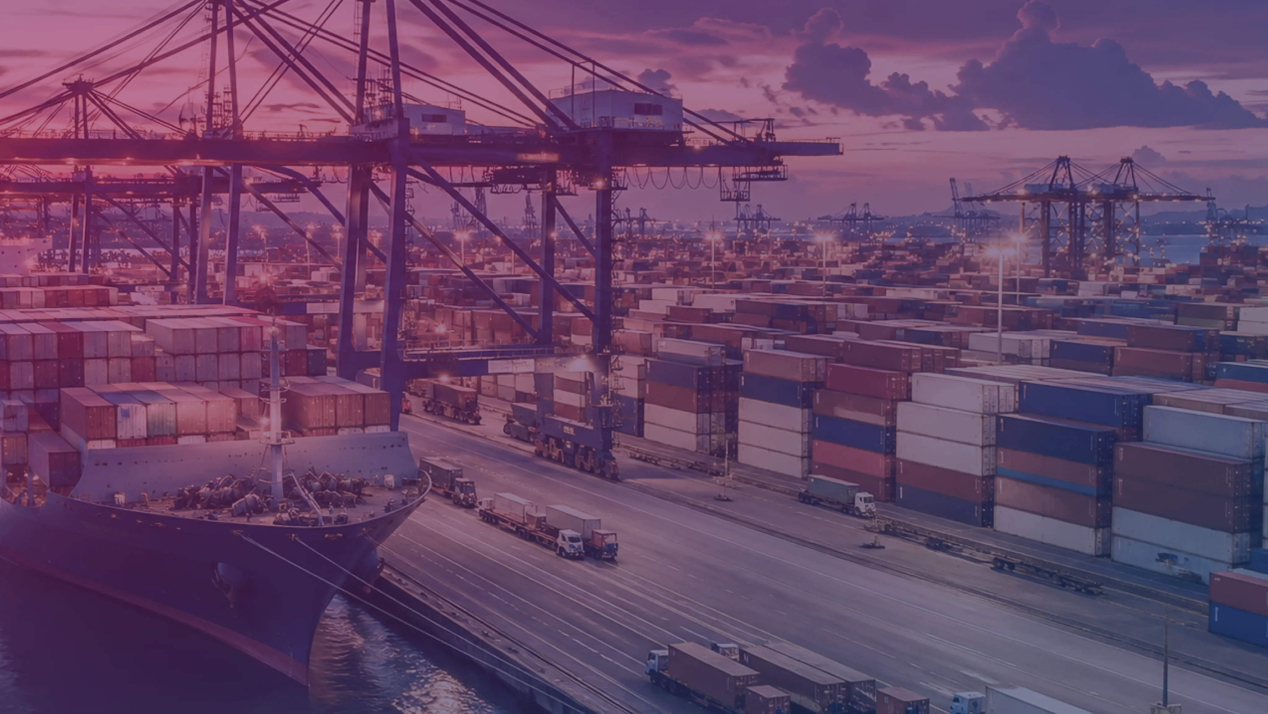Un terminal portuale al crepuscolo, con gru portacontainer, una nave cargo ormeggiata e cataste di container.